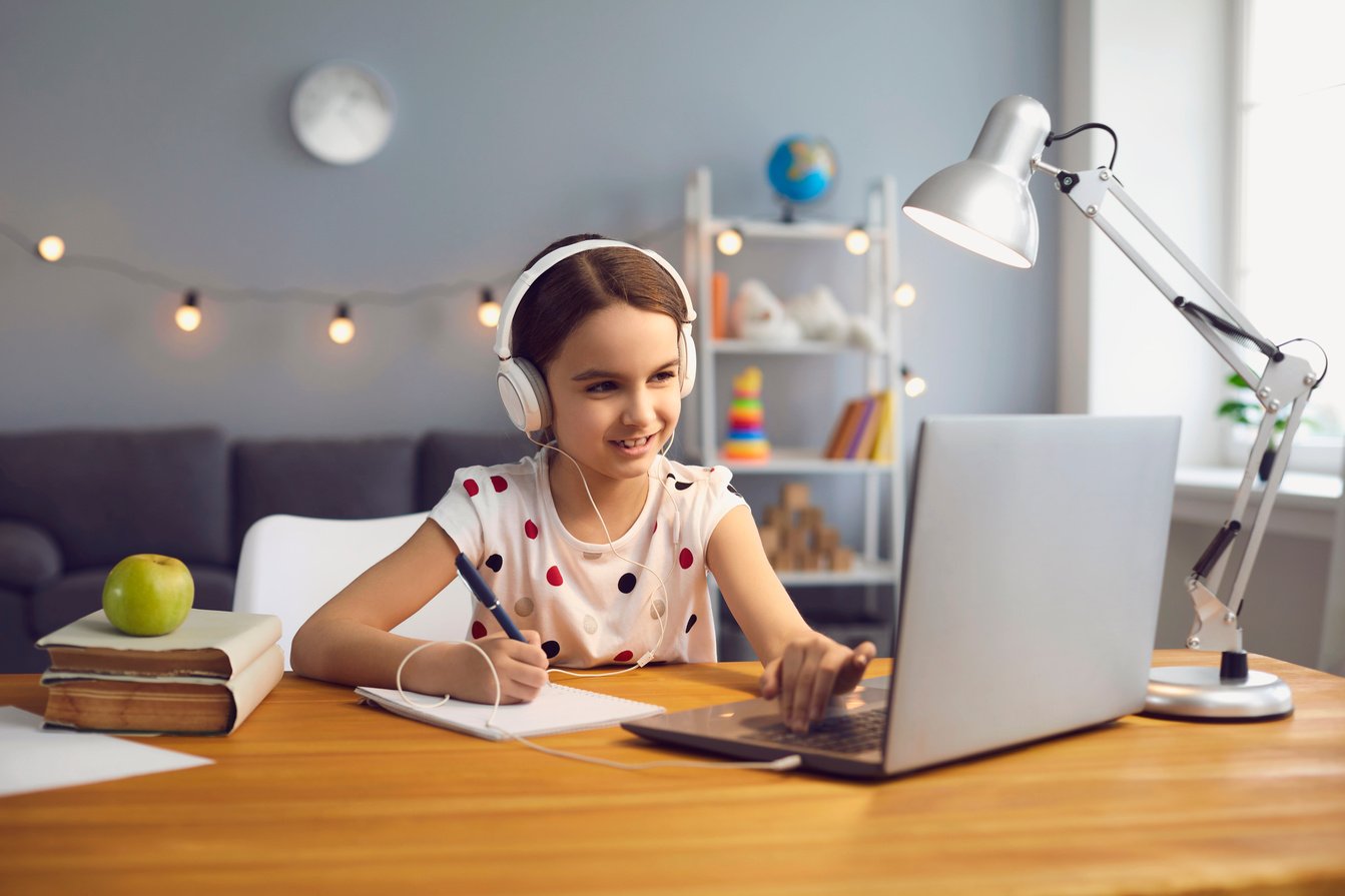 Home Online Schooling. Hardworking Little Girl in Headset Watching Online Lesson on Laptop